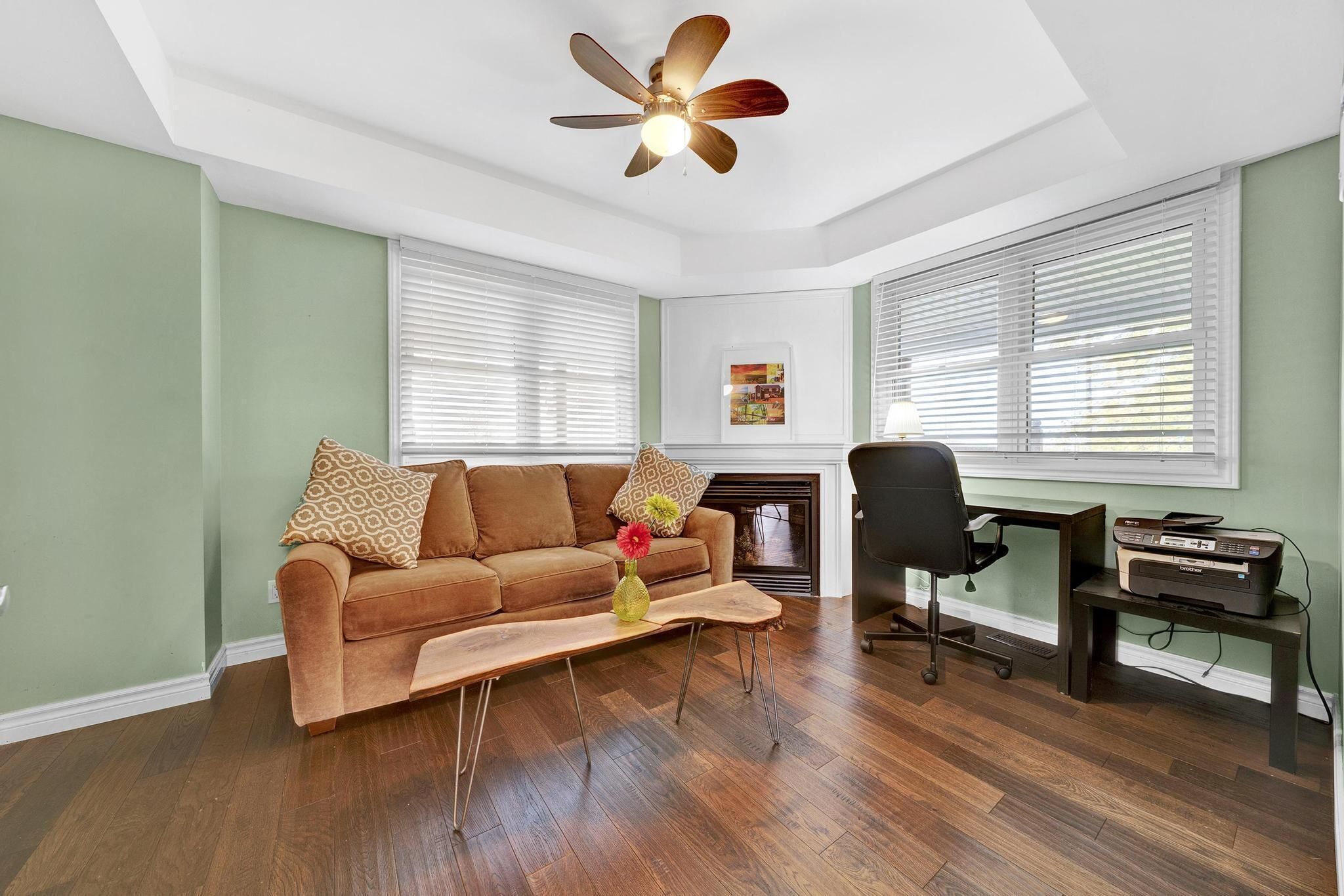 Un salon avec un canapé marron, une table basse, un fauteuil de bureau noir et un ventilateur de plafond.