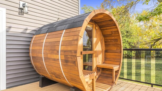 A wooden sauna structure with a bench inside, attached to a house with siding and a deck.