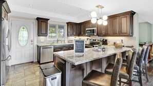 A modern kitchen with dark wood cabinets, stainless steel appliances, a marble island, and a chalkboard sign.