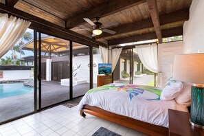 Ein Schlafzimmer mit Bett, Deckenventilator, Fernseher und Blick auf einen Swimmingpool.