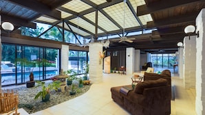 A spacious indoor area with a high ceiling, large windows, and a seating area with a brown sofa. - Private Oceanview Oasis w/Pool, Spacious Lanai, & Stunning Sunsets: Ono Oasis (Kailua Kona)