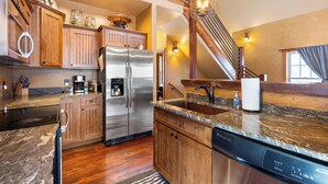 Una cocina con armarios de madera, electrodomésticos de acero inoxidable, encimera de granito y una escalera que sube a un nivel superior.