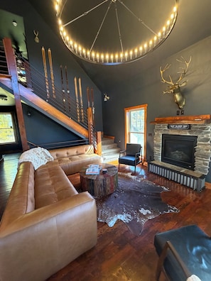 Ein geräumiges Wohnzimmer mit einer großen Ledersofa, einem Kamin aus Stein und einer Holztreppe.
