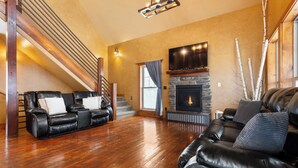 Una sala de estar amplia con chimenea, sofás de cuero y una escalera.