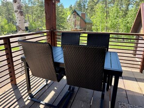Puisesta laudasta rakennettu terassi, jossa on pöytä ja kaksi tuolia, ja sen ympärillä on metallinen kaide.