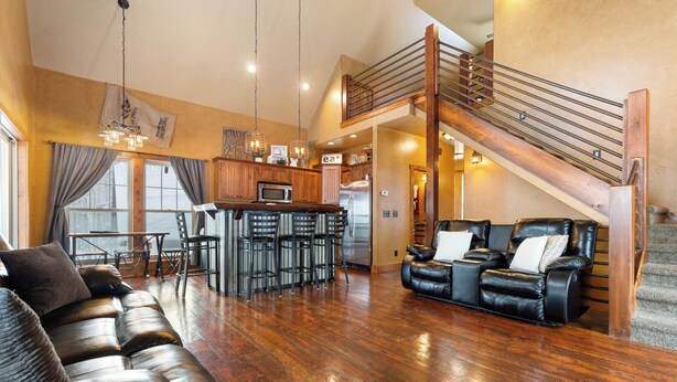 Amplia sala de estar con sofá de cuero, mesa de comedor con sillas, cocina con refrigerador y una escalera.