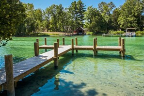 Un molo in legno si protende in acque limpide, circondato da alberi e una piccola capanna sullo sfondo.