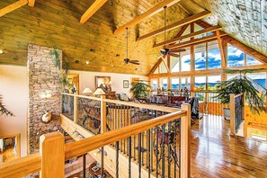 Un interior amplio con techo alto, vigas de madera, una pared de acento de piedra y ventanas grandes que ofrecen vistas.