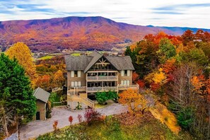A multi-story building with a prominent balcony, surrounded by autumn foliage and a mountainous backdrop. - Tanasi Lodge | Wake Up to Top-of-the-World Views | 10BR | Sleeps 30 (Sevier County)