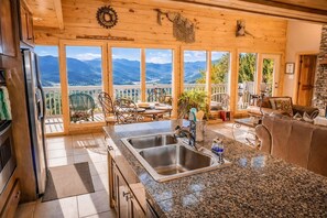 A kitchen with a granite countertop, stainless steel sink, and a view of mountains through large windows. - Tanasi Lodge | Wake Up to Top-of-the-World Views | 10BR | Sleeps 30 (Sevier County)