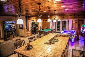 Un interior de madera con mesa de billar, máquinas de juegos y una larga mesa de comedor.