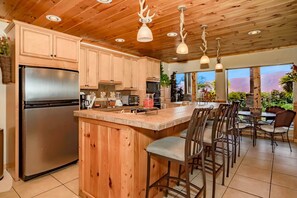 Una cocina con armarios de madera, un refrigerador de acero inoxidable, una isla central con taburetes altos y lámparas colgantes.