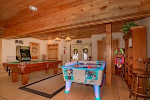 Una habitación con vigas de madera en el techo, una mesa de billar, una mesa de futbolín y un jukebox.