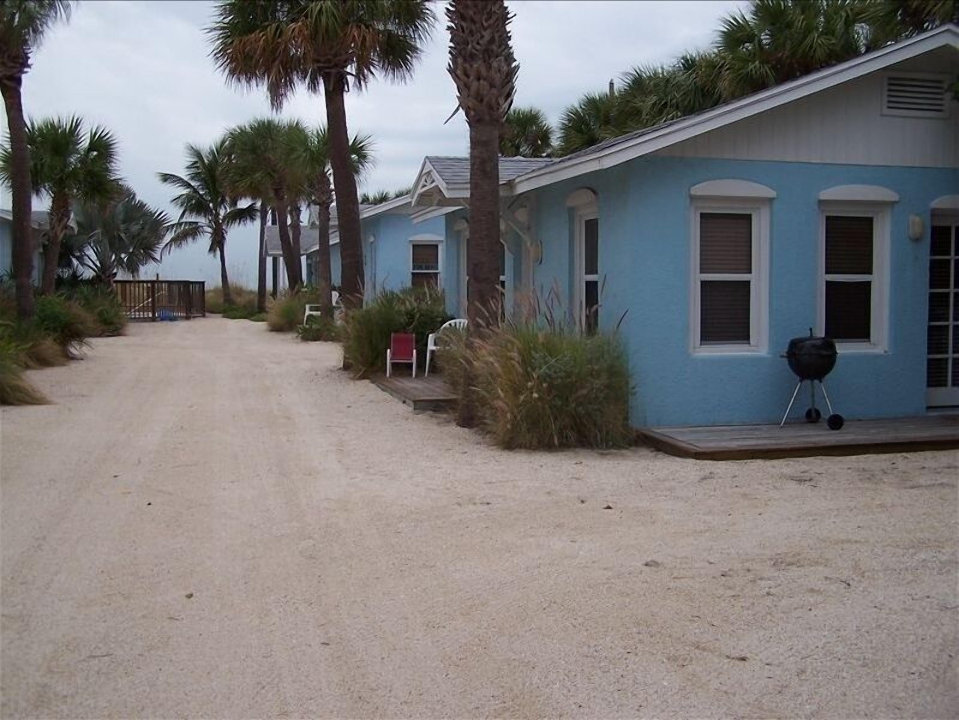 Een rij blauwe strandhuizen met een zandpad en palmbomen.