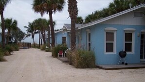 Reihenweise blaue Strandhäuser mit Kiesweg und Palmen.