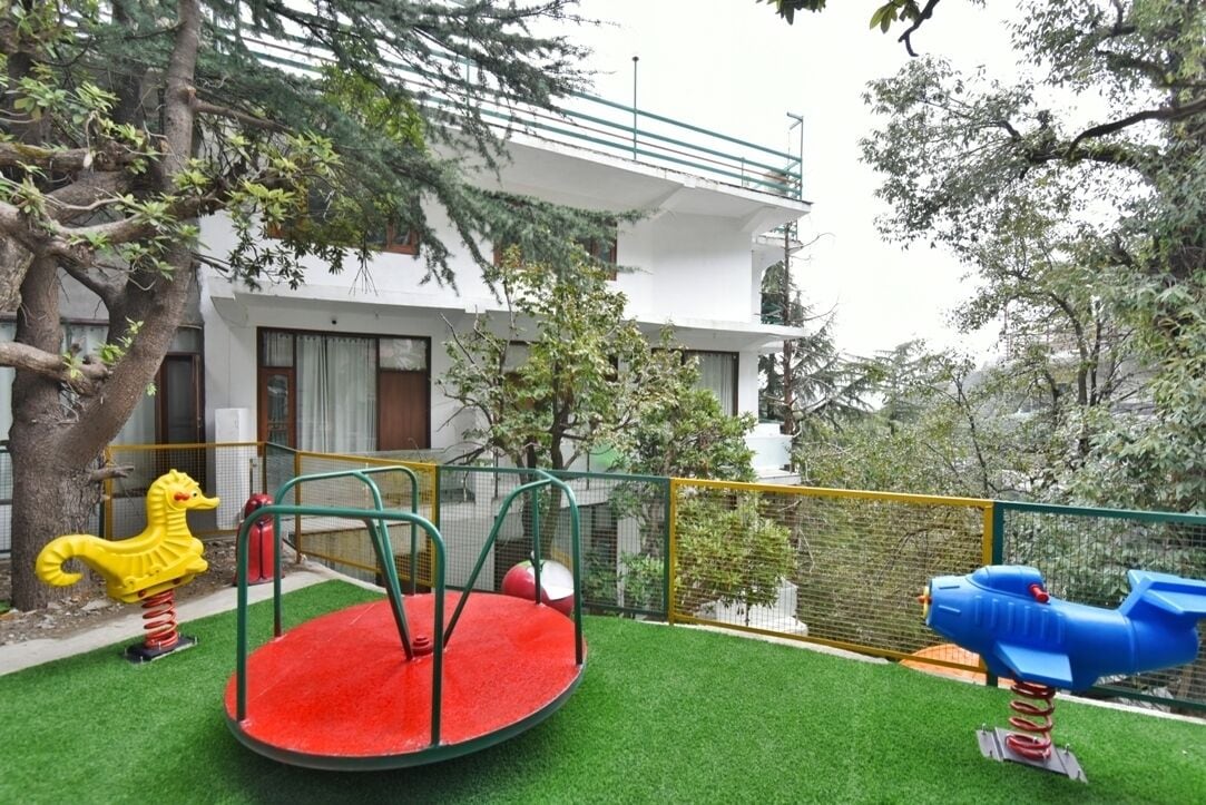 Un parque infantil con un carrusel rojo y un tobogán azul, rodeado por una cerca amarilla y árboles.