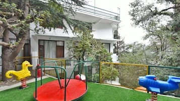 Un parque infantil con un carrusel rojo y un tobogán azul, rodeado por una cerca amarilla y árboles.