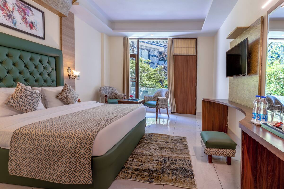 A hotel room with a large bed, a desk, a chair, a TV, and a balcony with a view.