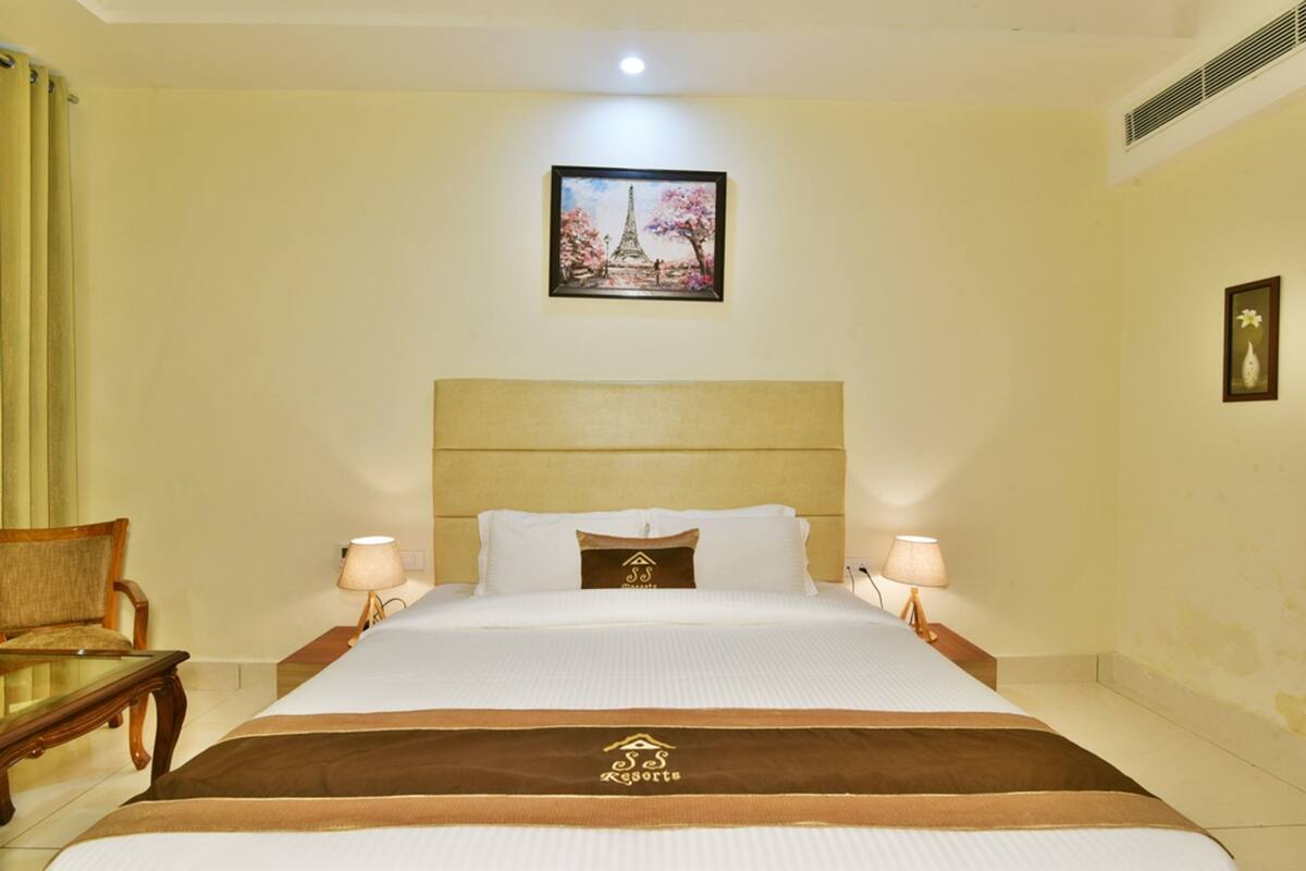 A hotel room with a bed, two bedside lamps, a chair, and a picture of the Eiffel Tower on the wall.