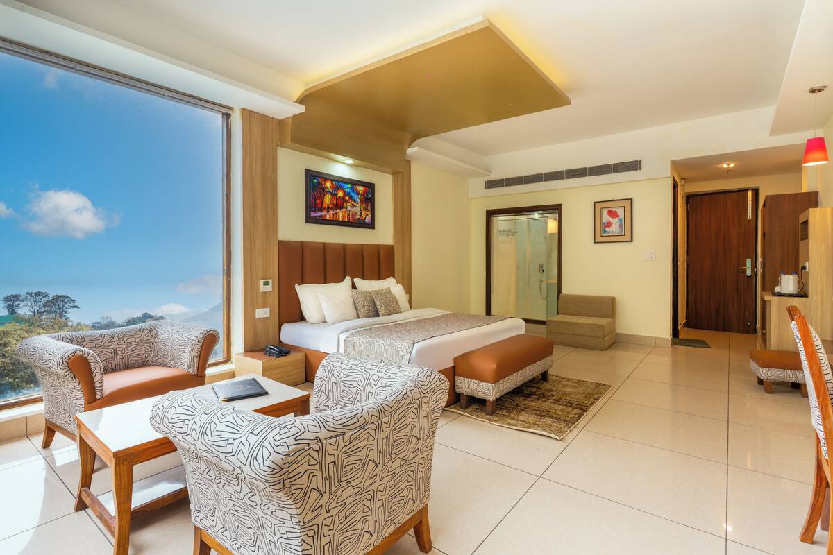A modern hotel room with a large bed, a sofa, a chair, a desk, and a view of the outdoors.