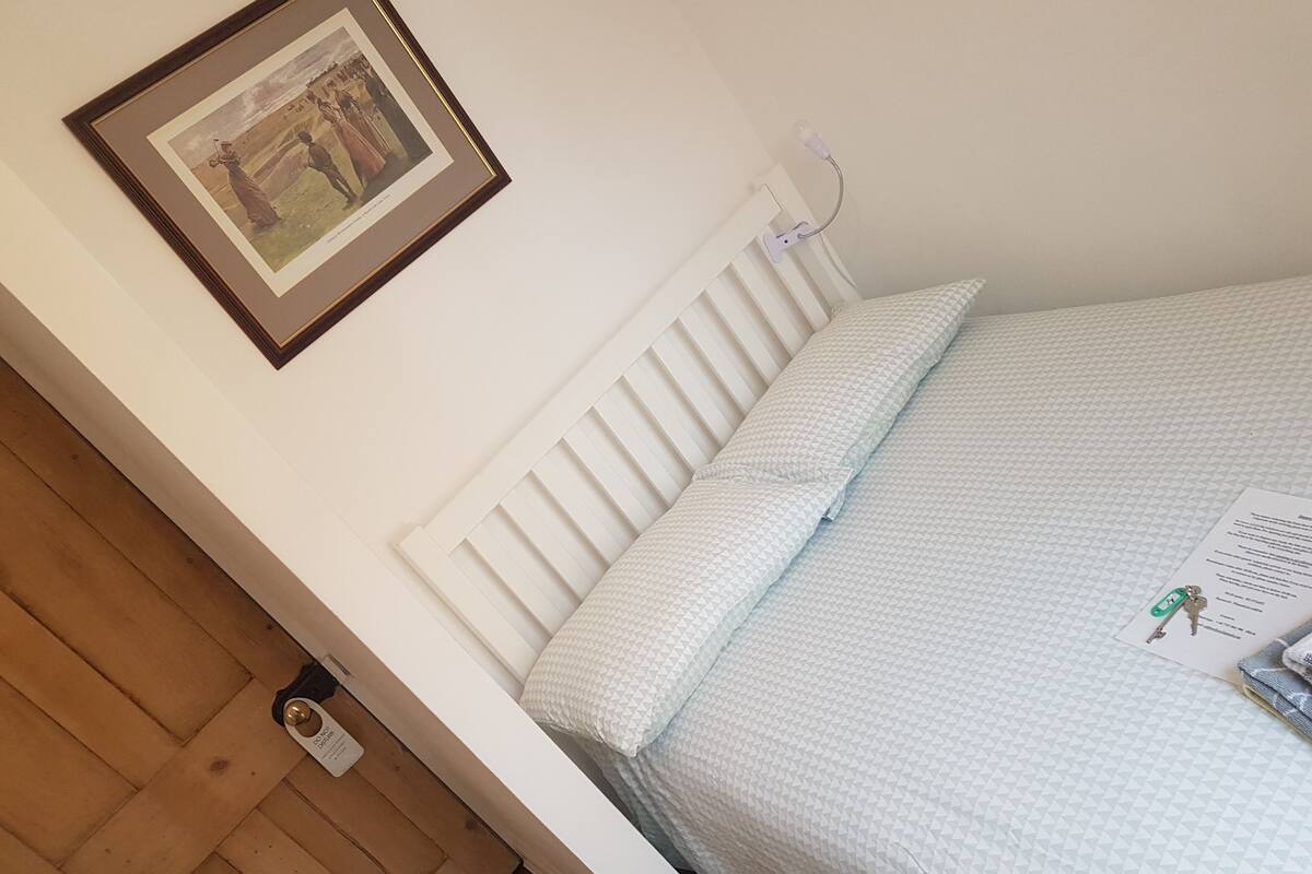 A bedroom with a white bed, a framed picture on the wall, and a bedside table with a lamp.