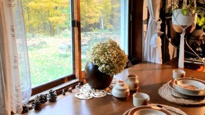 Una mesa de comedor dispuesta con platos, tazones y tazas de té, con una planta en maceta y una lámpara colgante.