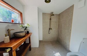 A bathroom with a shower, a wooden vanity with a bowl sink, and a framed picture on the wall.