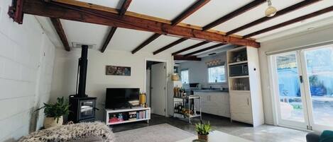 Una sala de estar con sofá, mesa de centro, televisor y chimenea. Se ve una cocina a través de una puerta abierta.