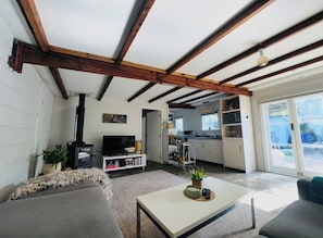 A living room with a sofa, a coffee table, a TV, and a fireplace. There is a kitchen visible through an open door.