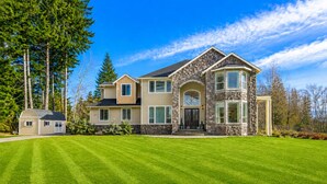 A large two-story house with a stone facade, a well-maintained lawn, and a small shed.