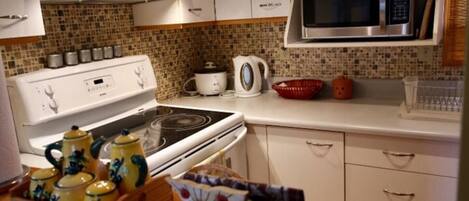 A kitchen with white cabinets, a stove, a microwave, and a tiled backsplash.