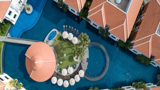 Vista aérea de un resort con múltiples piscinas, una piscina circular central y áreas de descanso circundantes con sombrillas.