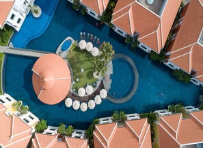 An aerial view of a resort with multiple swimming pools, a central circular pool, and surrounding lounge areas with umbrellas. - The Royal Family Suites by Memoire Palace Resort & Spa (Siem Reap)
