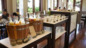 Montaje de bufé con diversas opciones de comida y bebida, incluyendo zumo fresco de sandía y zumo de naranja, exhibido sobre barriles de madera y platos blancos.