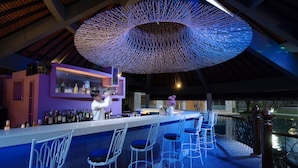 Zona de bar con diseño moderno, que destaca una lámpara de techo única, taburetes y una variedad de botellas en los estantes.