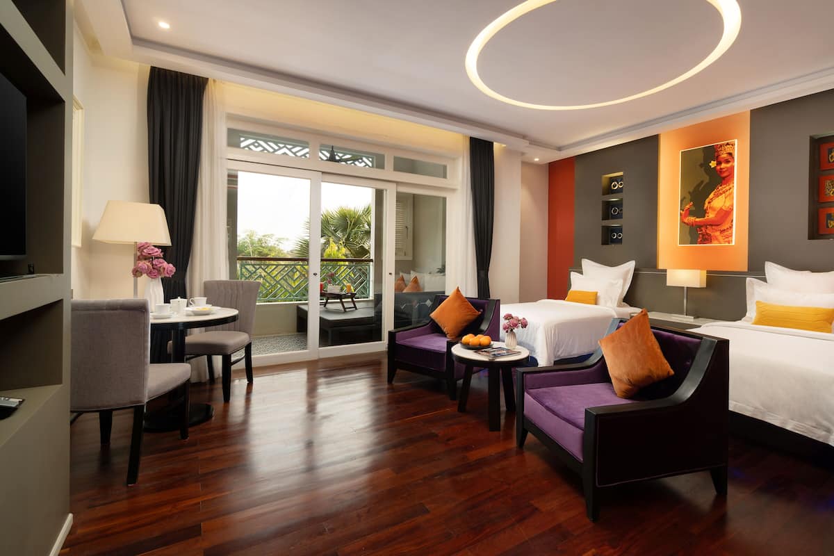 A hotel room with a balcony, a dining area, and a bed with multiple pillows.