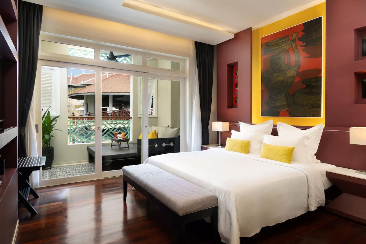 A hotel room with a large bed, a bench, a desk, and a view of the outside balcony.