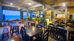 A restaurant with wooden tables and chairs, a view of the ocean, and a bar area. - Apartment By Sunrise Resort (Ko Pha-ngan)