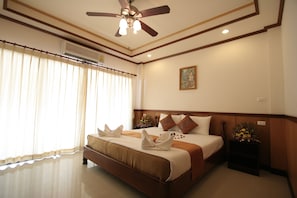 A hotel room with a large bed, a ceiling fan, an air conditioning unit, a nightstand with a vase of flowers, and a painting on the wall. - Apartment By Sunrise Resort (Ko Pha-ngan)