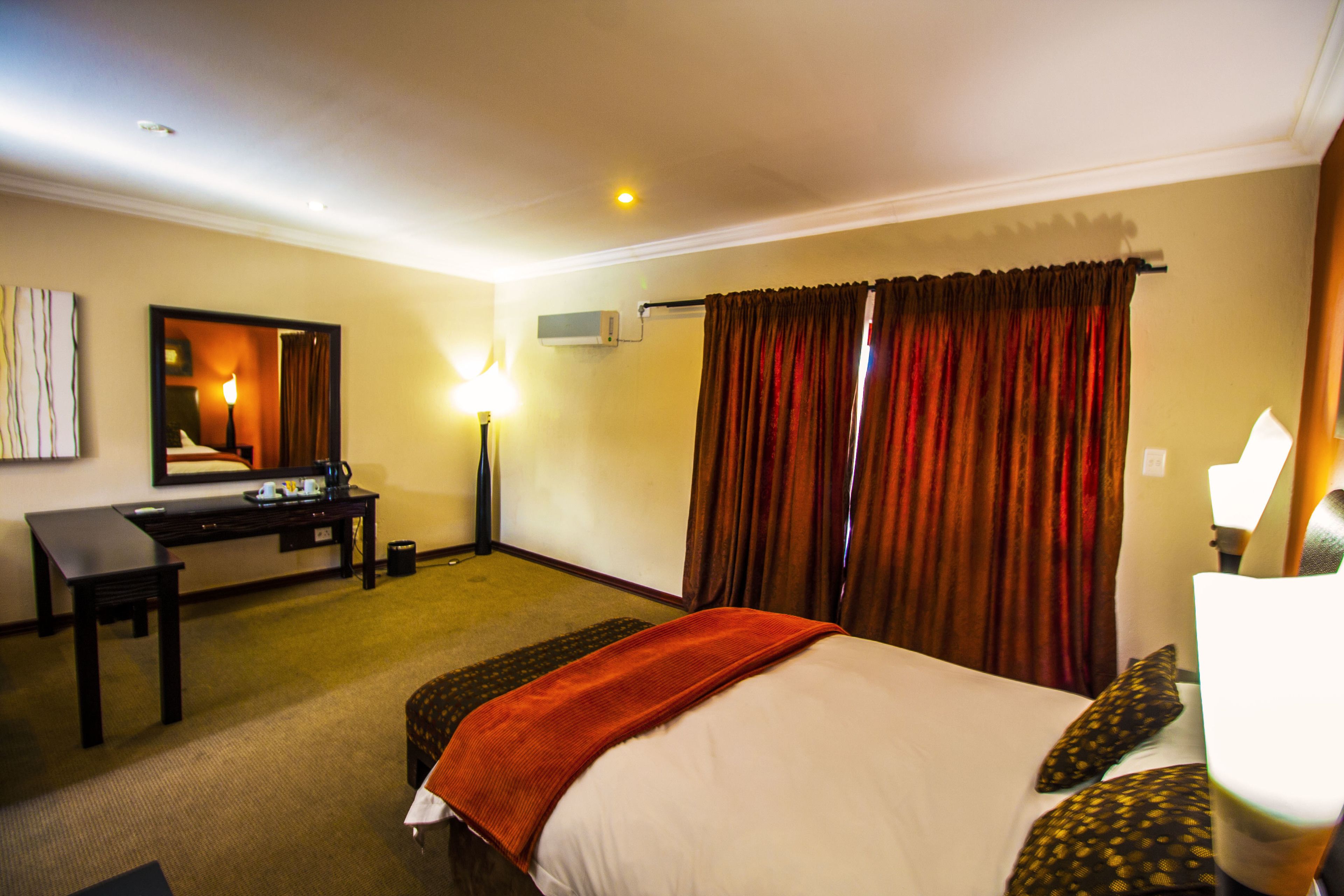 Habitación de hotel con cama, escritorio, silla, lámpara y ventana con cortinas.