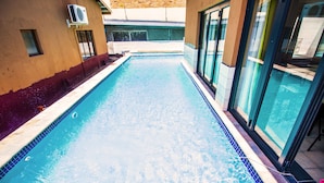 A swimming pool with clear blue water, surrounded by a tiled deck and glass doors leading to a covered area. - Coyotes Hotel and Conference Centre (Mbombela)
