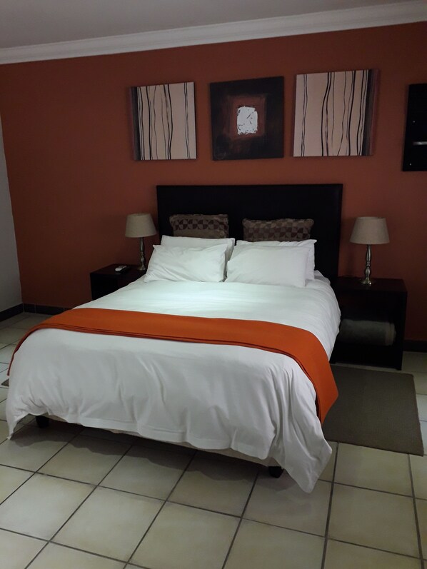 A hotel room with a large bed, two bedside tables, and a nightstand. - Coyotes Hotel and Conference Centre (Mbombela)