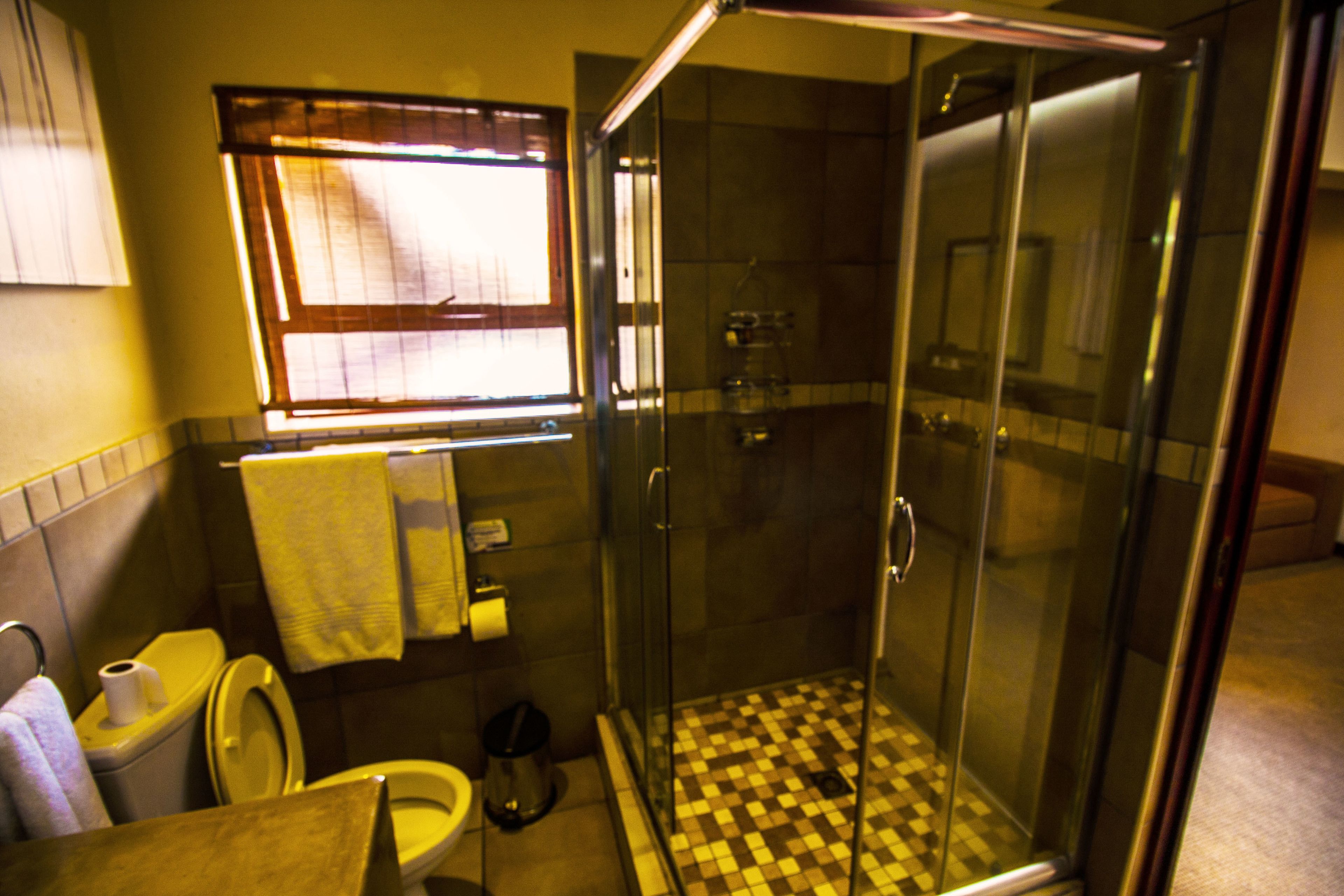 Un baño con ducha de vidrio, inodoro y ventana con persianas.