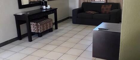A hotel room with a bed, a desk with a chair, a sofa, a window with curtains, and a wall-mounted mirror.