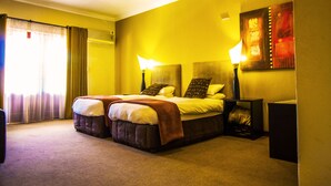 A hotel room with a large bed, two bedside lamps, a nightstand, and a painting on the wall. - Coyotes Hotel and Conference Centre (Mbombela)