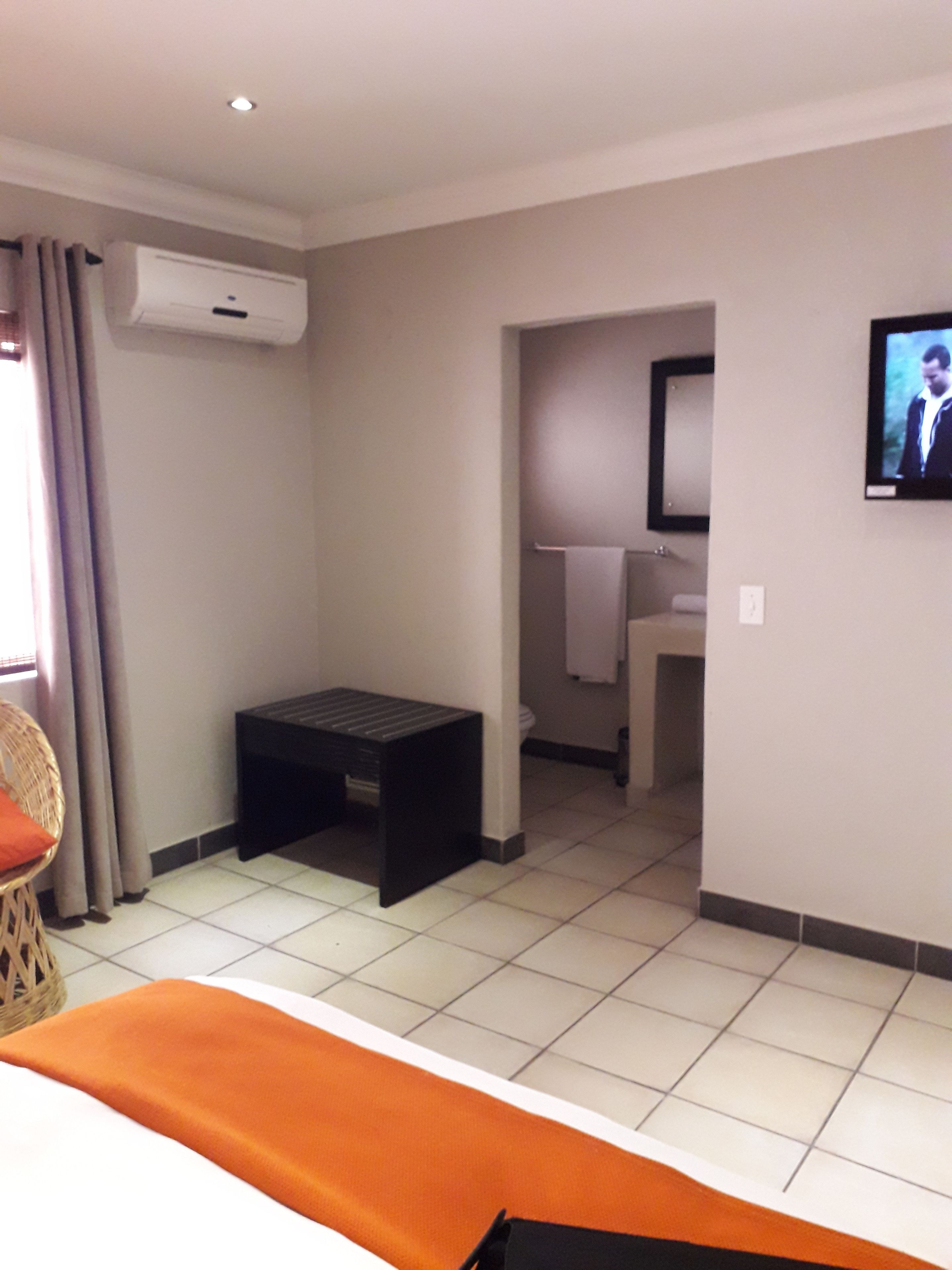 A hotel room with a bed, a small table, a TV, and a bathroom visible through an open door.