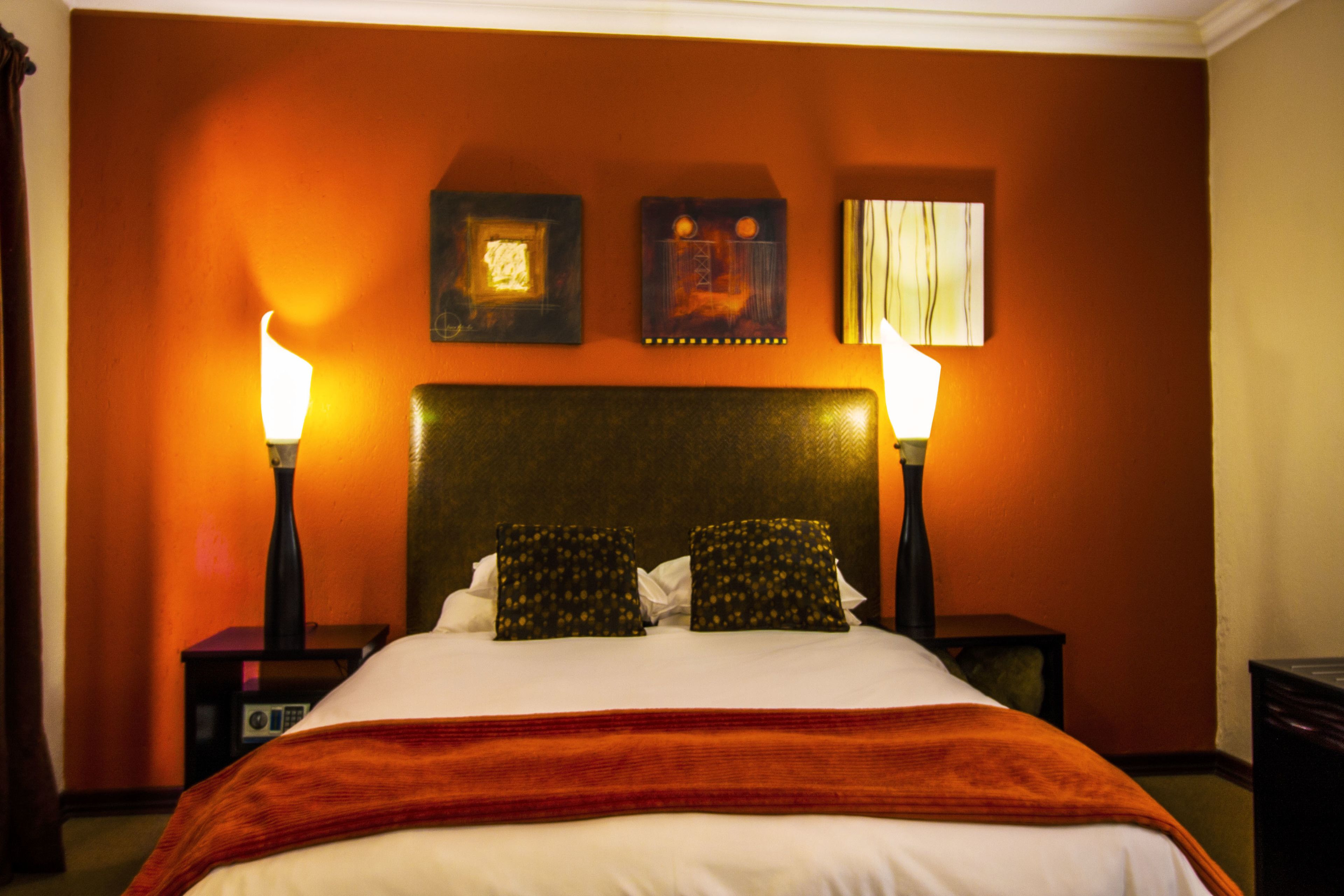 A hotel room with a large bed, two bedside lamps, a headboard, and two framed pictures on the wall.