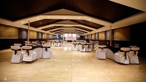 Un salón amplio con filas de mesas y sillas, un techo alto con iluminación empotrada y un suelo pulido.