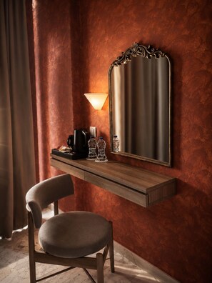 Ein Hotelzimmer mit einem Holztisch, einem Stuhl, einem Spiegel, einer Lampe und einer Kaffeemaschine.
