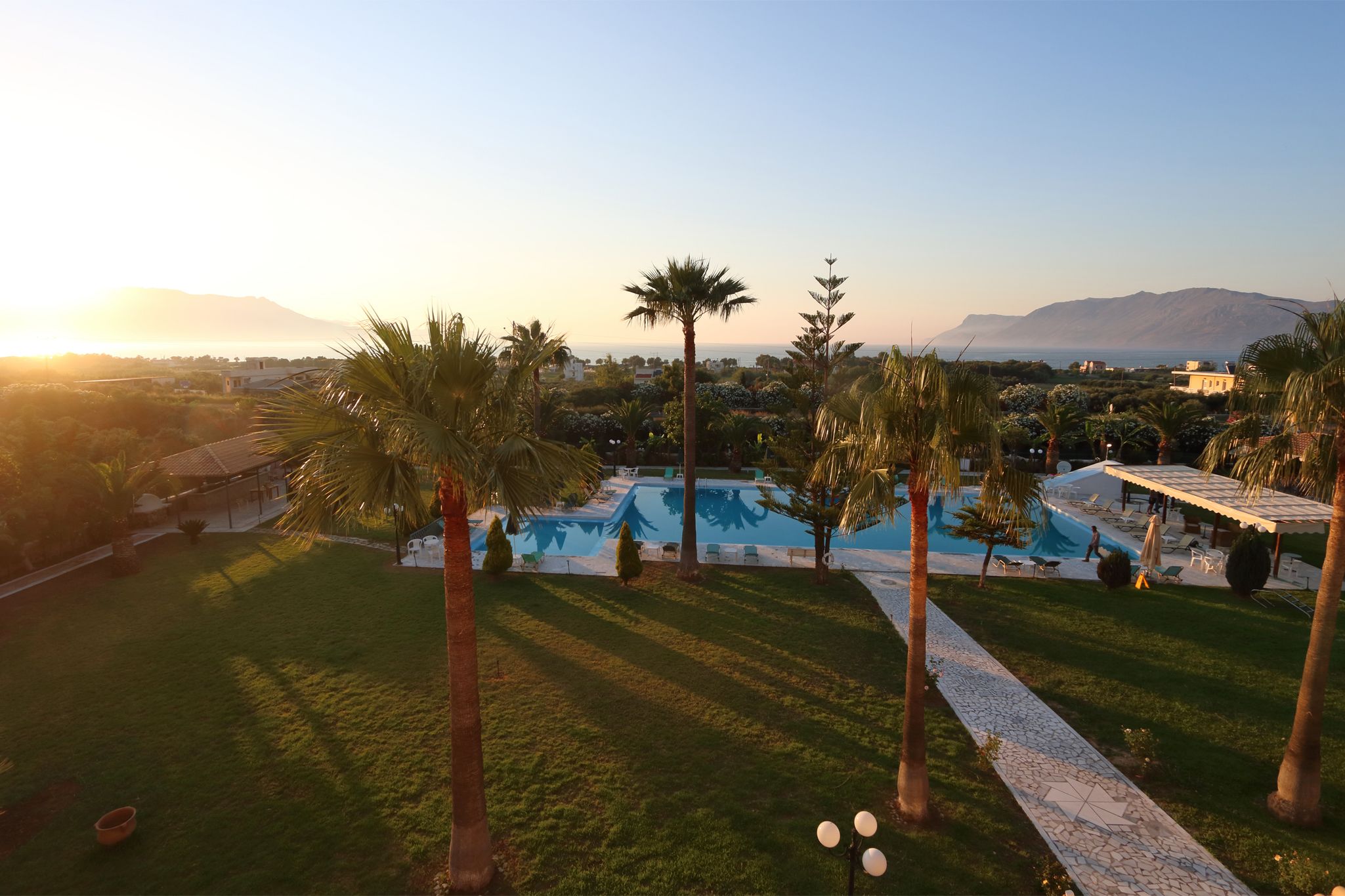 A pool area with palm trees, a tiled pathway, and a view of distant mountains.